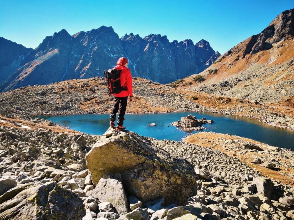 Sinnbild für äußere Ressource, hier kahle Berglandschaft mit blauem Himmel und See und Wanderer, auf einem Felsbrocken stehend